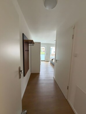 Un pasillo con suelo de madera y paredes blancas, que conduce a una habitación con cama y vistas al exterior.