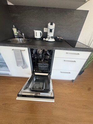 A modern kitchen with a built-in dishwasher, a kettle, and a coffee maker on the countertop.