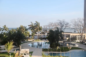 Zona de piscina en un resort, con palmeras, sillas de descanso y vista al océano.