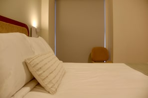 Una habitación de hotel con una cama, almohadas, una silla y un aplique de pared.