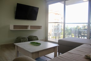 Una sala moderna con un televisor de pantalla plana montado en la pared, una mesita con un objeto verde encima, dos sillones y un sofá.
