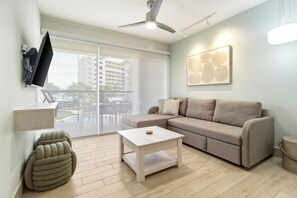 A modern living room with a sofa, a coffee table, a television mounted on the wall, and a ceiling fan. - Casa Flick New 3 BR 2 Bath Oceanfront Resort Condo (Chame)
