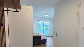 A hallway with a bed in the background, a door on the right, and a ceiling light.