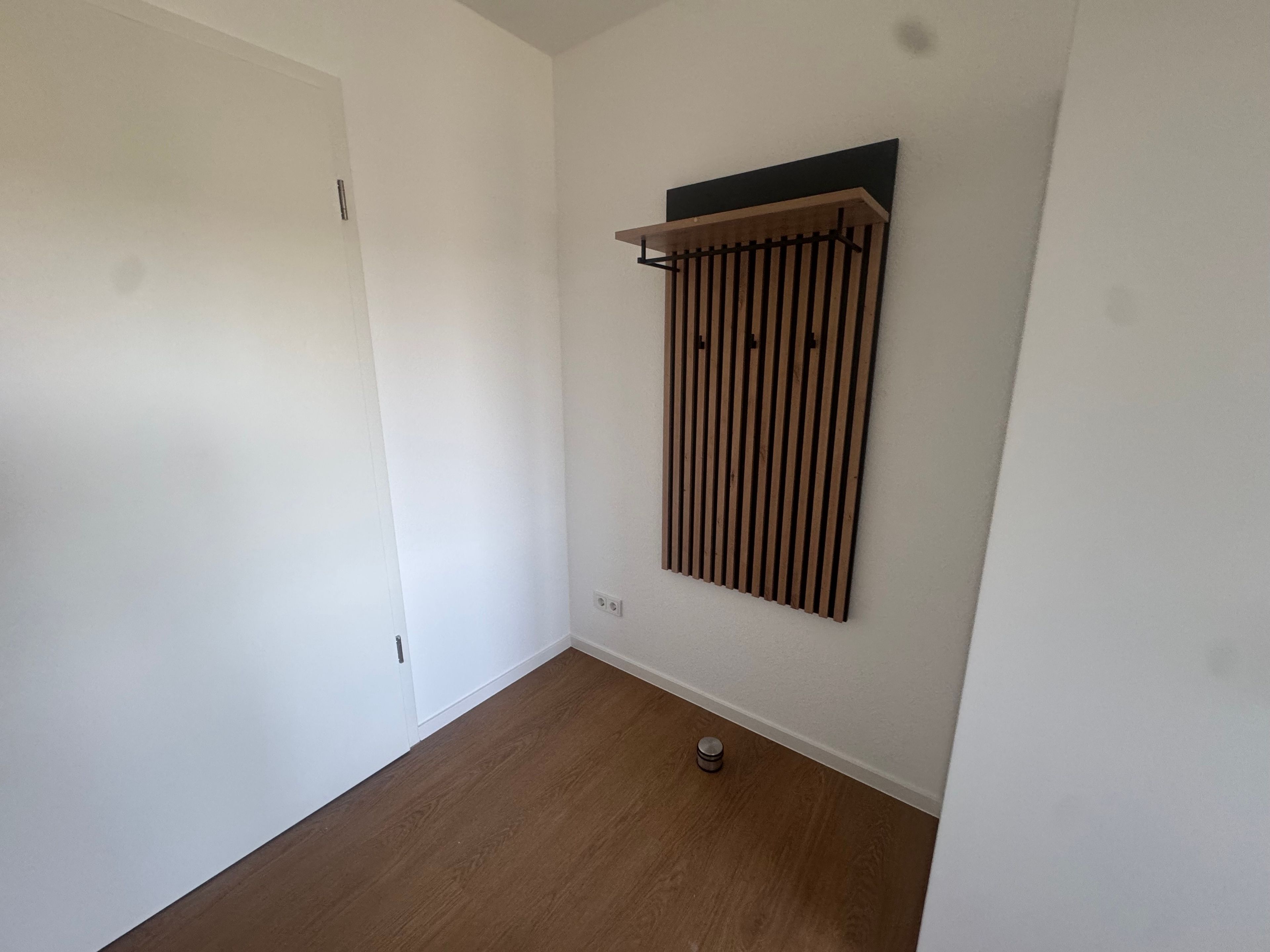 Ein Zimmer mit einer weißen Tür, einem Holzboden und einem an der Wand befestigten Ablagefach.
