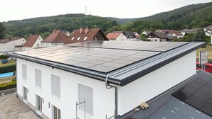 Um edifício com telhado plano, janelas amplas e piscina visível ao fundo.