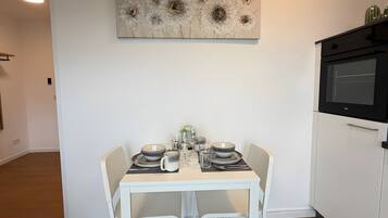 Un'area pranzo con un tavolo bianco apparecchiato per due, una cucina moderna con un forno nero e un elemento decorativo sopra il tavolo.