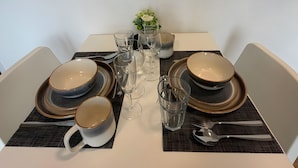 Uma mesa posta com pratos, tigelas, copos e talheres, com um vaso de flores no centro.