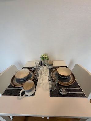 Ein Tisch ist mit Tellern, Schüsseln, Gläsern und Besteck gedeckt, in der Mitte steht ein Blumenstrauß.