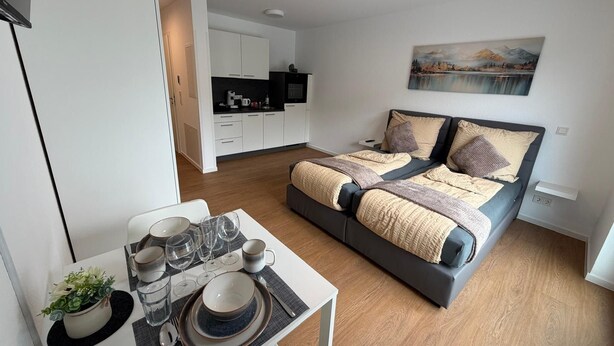 A modern bedroom with a bed, a dining table with set table, and a kitchen in the background. - Apartment in A Hotel 'Werner Apartments Mecklar 9' with Shared Terrace, Shared Garden and Wi-Fi (Ludwigsau)