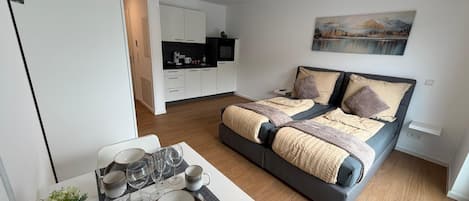 Une chambre à coucher moderne avec un lit, une table à manger dressée et une cuisine en arrière-plan.