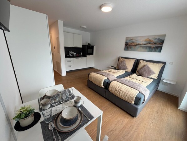 Ein modernes Schlafzimmer mit einem Bett, einem Esstisch mit gedecktem Tisch und einer Küche im Hintergrund.