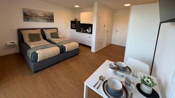 Un appartement moderne doté d’un lit double, d’une kitchenette, d’un coin repas et d’un tableau au mur.