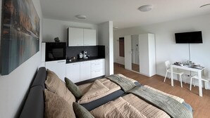 Une chambre moderne dotée d’un grand lit, d’une kitchenette, d’un coin repas et d’un téléviseur fixé au mur.