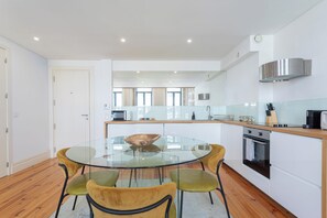A modern kitchen with a glass dining table, wooden chairs, and a stainless steel range hood. - Sweet Escape | Charming One-Bedroom Apartment in the Heart of Porto (Porto)