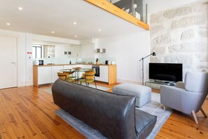 A modern living room with a sofa, a TV, and a stone wall. - Sweet Escape | Charming One-Bedroom Apartment in the Heart of Porto (Porto)