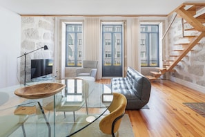 A modern living room with a glass coffee table, leather sofa, and a wooden dining table. - Sweet Escape | Charming One-Bedroom Apartment in the Heart of Porto (Porto)