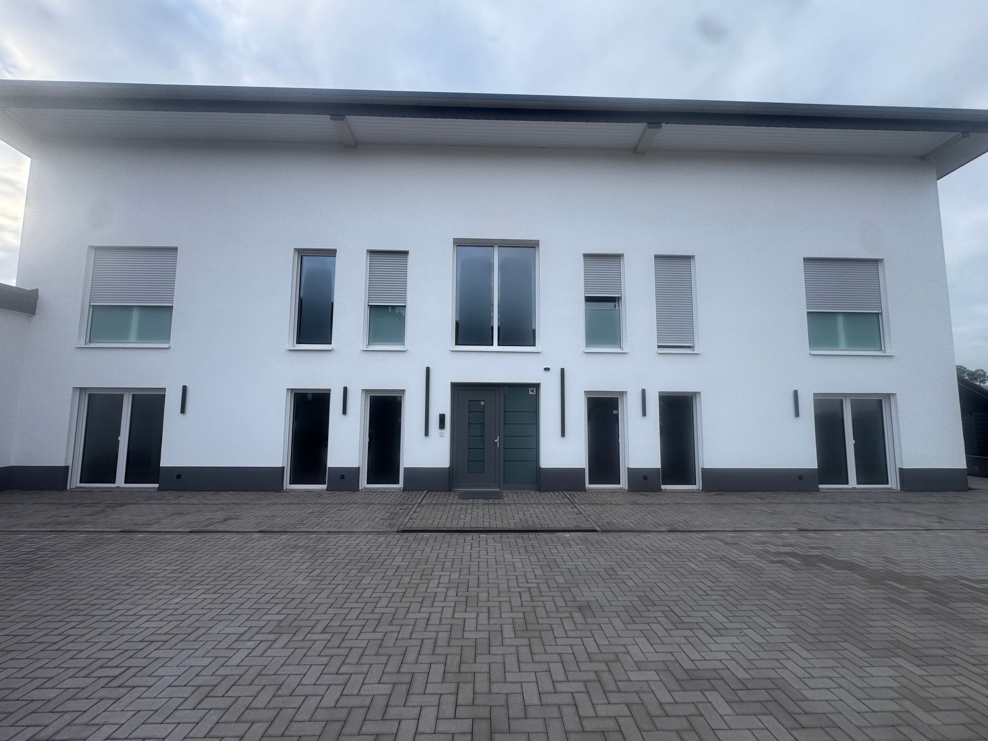 Ein modernes Gebäude mit einer symmetrischen Fassade, zahlreichen Fenstern und einem zentralen Eingang.