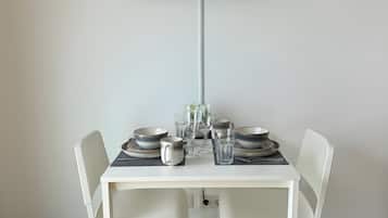 Un coin repas avec une table dressée pour deux personnes, un téléviseur à écran plat fixé au mur et des chaises blanches.