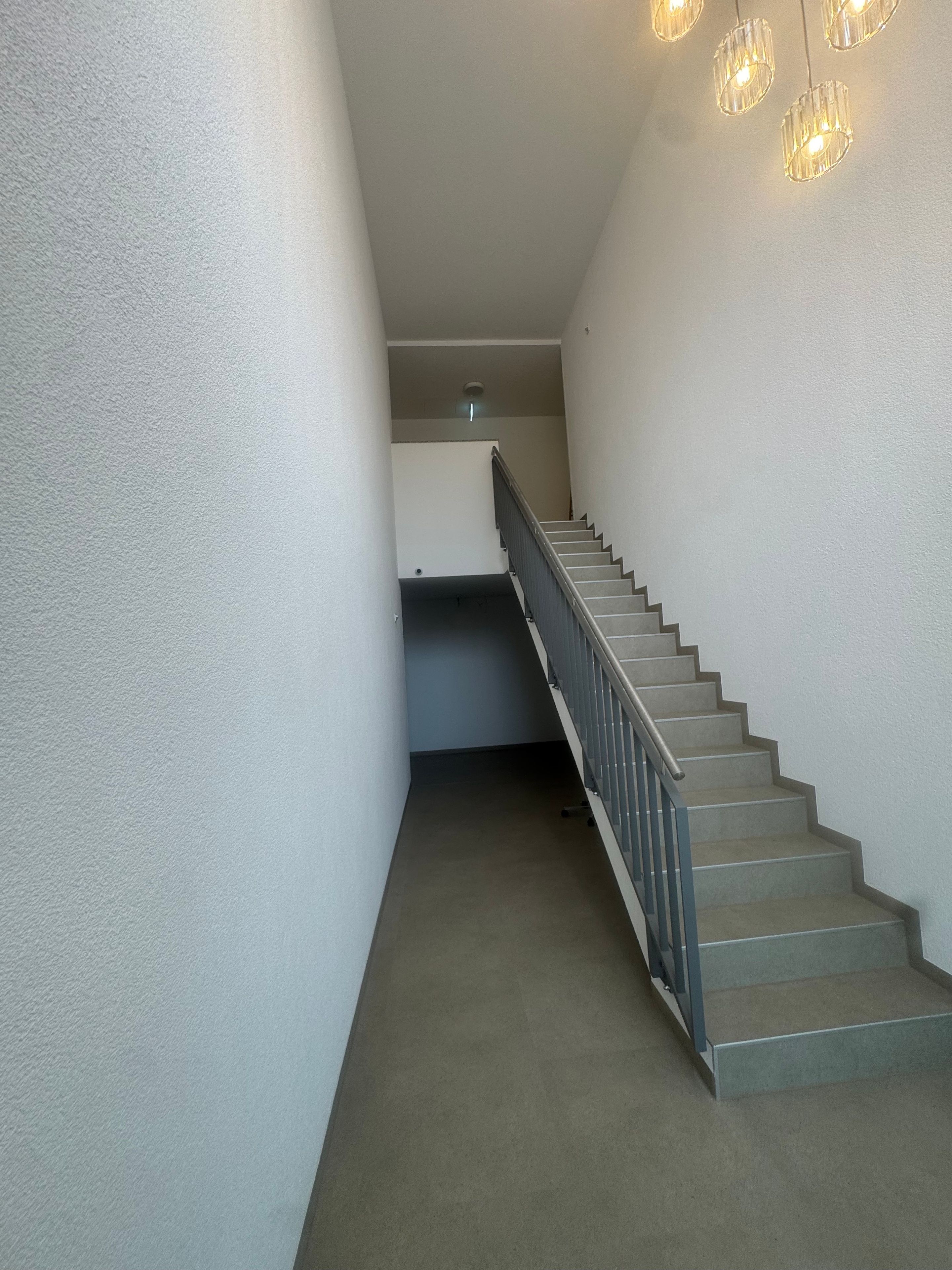 Eine Treppe mit Metallgeländer und Teppichstufen, die zu einer Zwischenebene mit einer Leuchte führen.