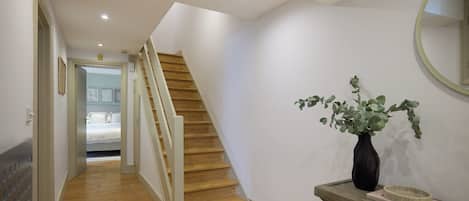 Un pasillo con una escalera de madera, un espejo y una planta en maceta.