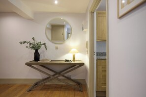 Ein Flur mit einem Holztischchen, einem Blumentopf, einer Lampe und einem Spiegel an der Wand.