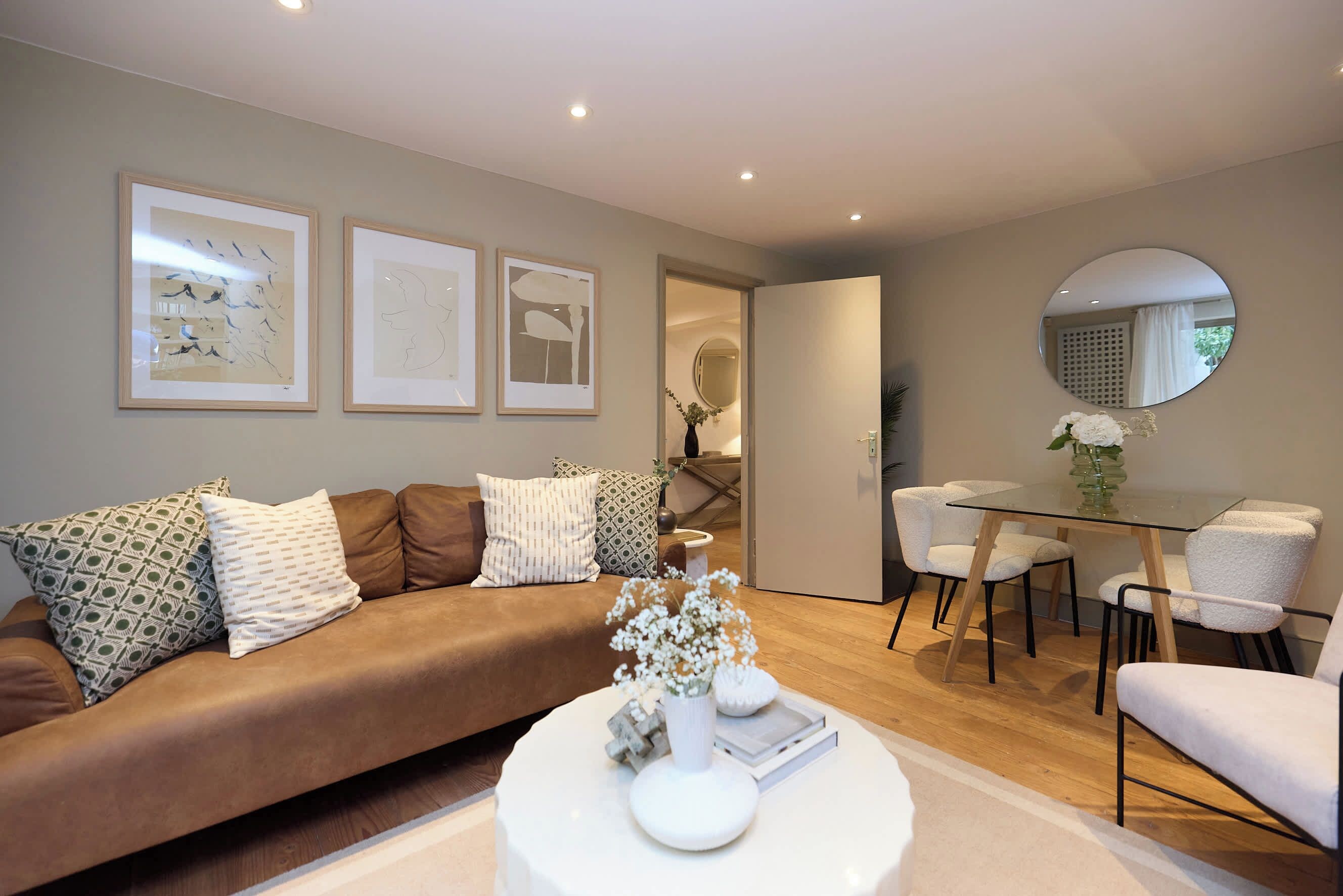 Una sala de estar moderna con un sofá marrón, una mesa de centro de vidrio y un comedor con una mesa de vidrio y sillas blancas.