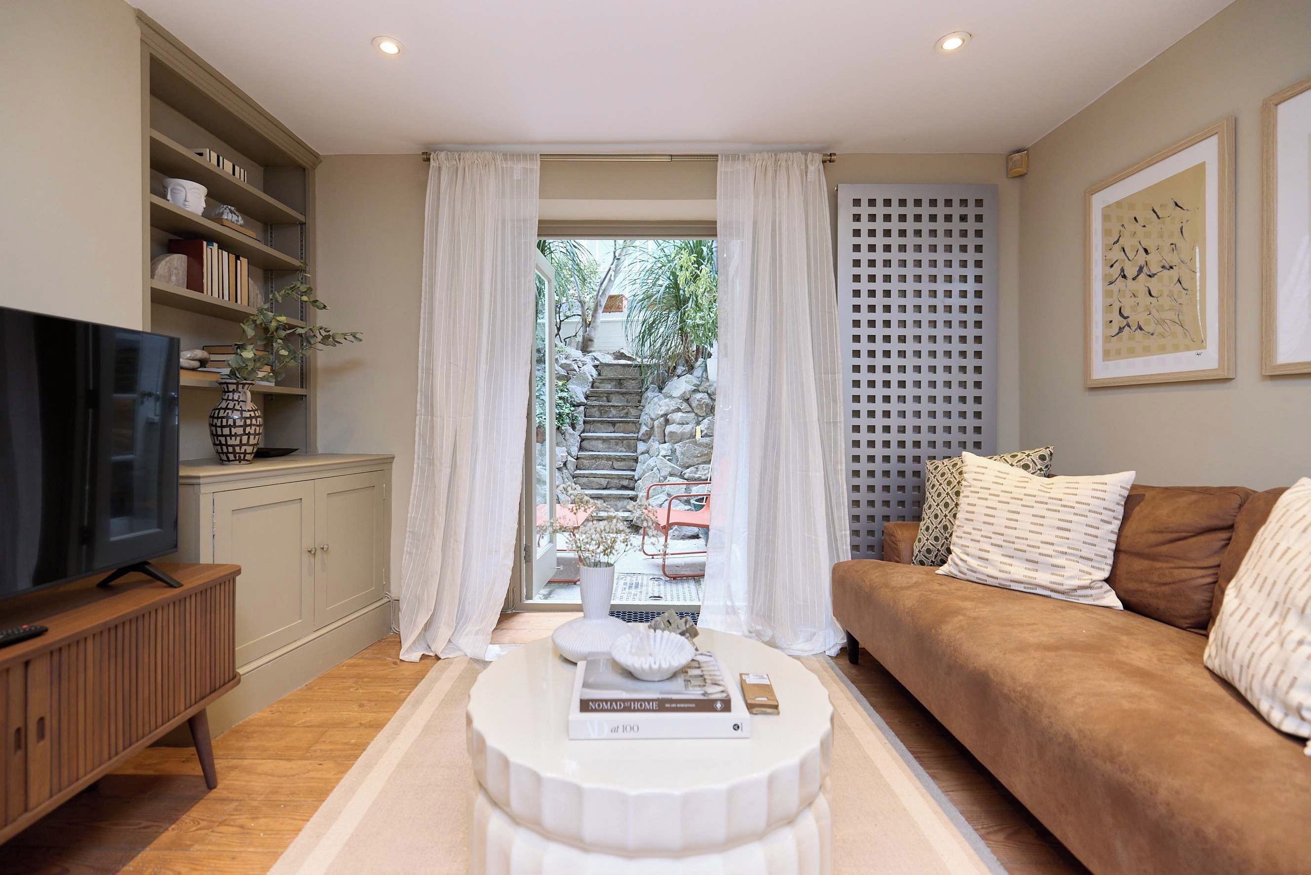 Una sala de estar con televisor, sofá, mesa de centro y estantería. Se ve un jardín a través de un ventanal.