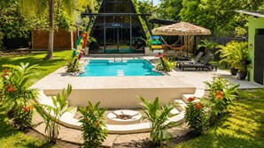 Una piscina rodeada de exuberante vegetación y una estructura con techo de paja.