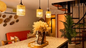 Una cocina con encimeras de granito, lámparas colgantes, una isla central con un jarrón de flores secas y una escalera al fondo.