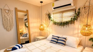 Una cama bien hecha con colcha a cuadros, una mesita de noche con lámpara y un aire acondicionado de pared.