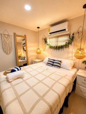 Un letto rifatto con una coperta a quadri, un comodino con una lampada e un condizionatore d'aria fissato al muro.