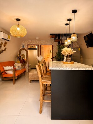 Una cocina moderna con una isla central, iluminación colgante y un comedor con sillas de madera.