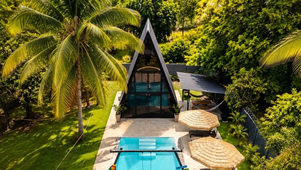 Una villa moderna con piscina, rodeada de exuberante vegetación y palmeras.