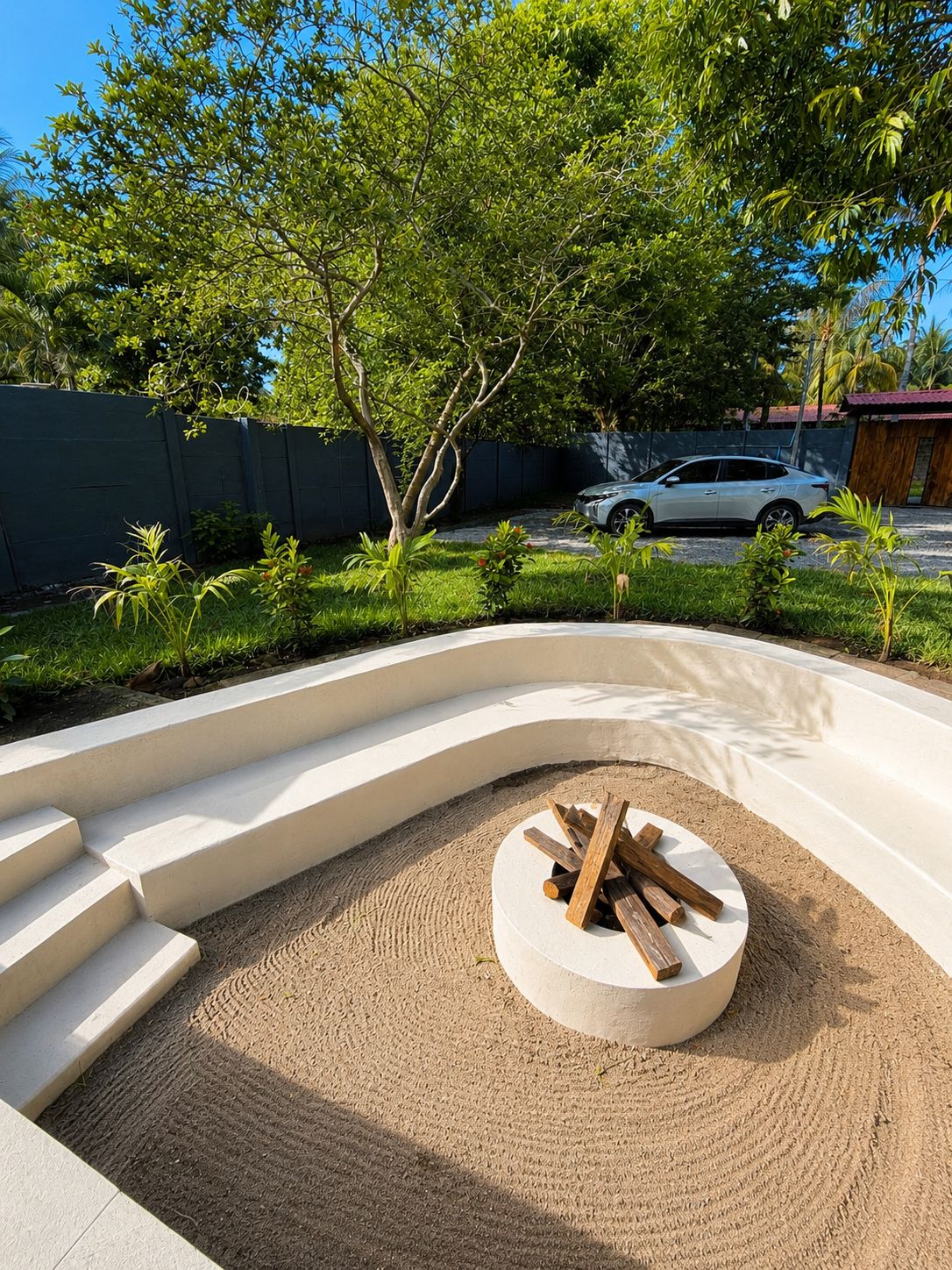 A landscaped outdoor area with a circular seating area, steps leading up to it, and a white car parked in the background.