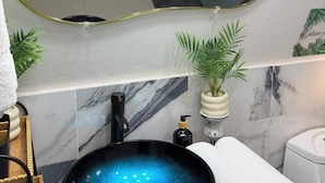 Un baño con un lavabo negro tipo recipiente, un espejo con marco dorado, un inodoro blanco y un perchero para toallas.