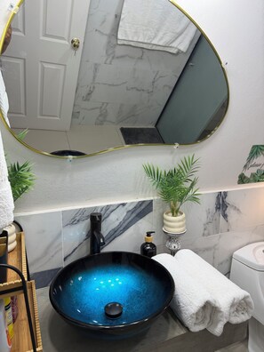 Un bagno con un lavabo nero a incasso, uno specchio con cornice dorata, un water bianco e un porta asciugamani.