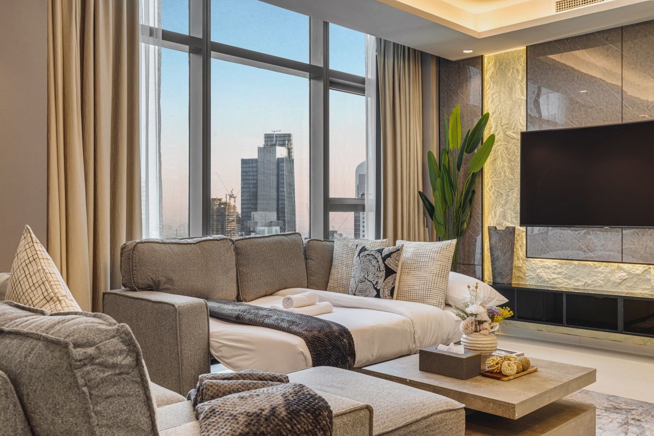 A modern living room with a large window, a flat-screen TV, and a sofa set.