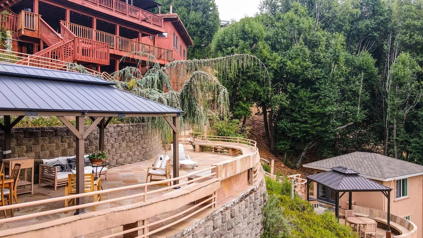 A multi-level outdoor area with stone steps, wooden furniture, and a red building in the background.