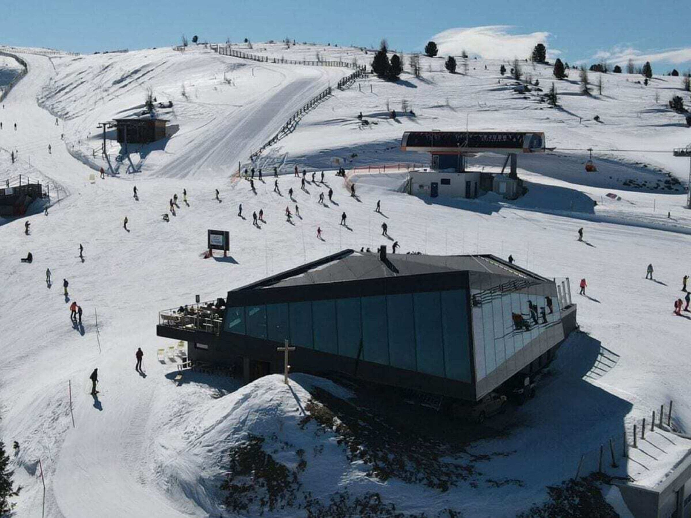A ski resort with a large glass building, ski slopes, and a fence.