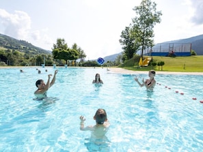 Piscina com várias pessoas na água, rodeada por um espaço gramado e árvores.
