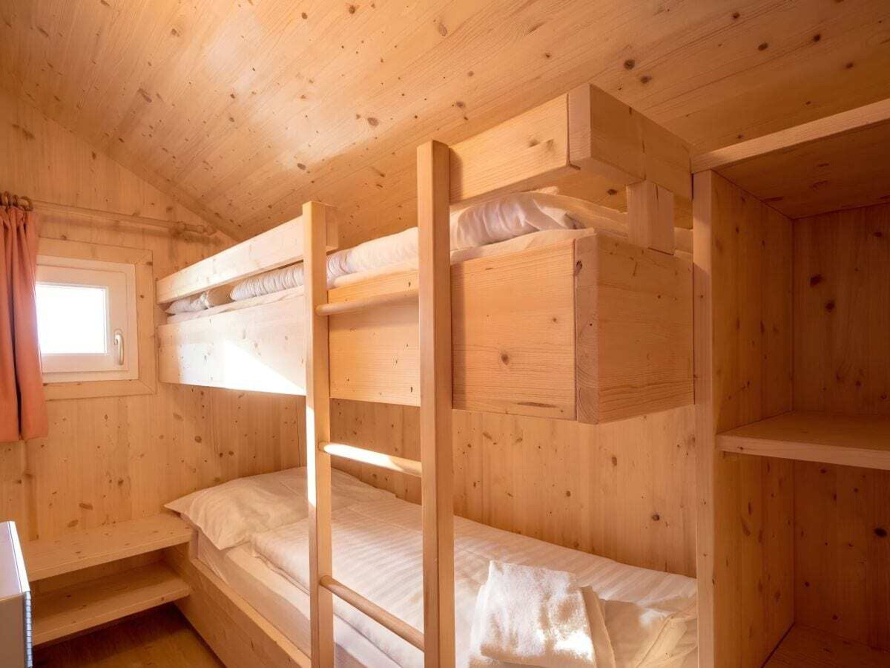 Een houten hut met stapelbedden, een raam met gordijnen en een klein tafeltje.
