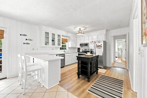 A modern kitchen with white cabinetry, a central island, and a black bar stool. - Little Minnow - 3 Bedrooms - Mainland (Pawleys Island)