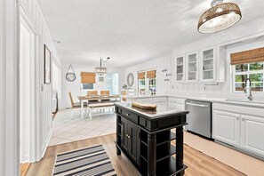 A modern kitchen with white cabinetry, a black island, and a hanging light fixture. - Little Minnow - 3 Bedrooms - Mainland (Pawleys Island)