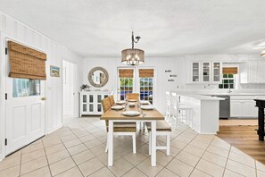 A spacious kitchen with white cabinetry, a dining area with a wooden table and chairs, and a hanging light fixture. - Little Minnow - 3 Bedrooms - Mainland (Pawleys Island)