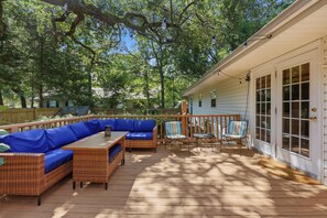 An outdoor patio with a long blue sofa, a wicker table, and striped chairs. - Little Minnow - 3 Bedrooms - Mainland (Pawleys Island)