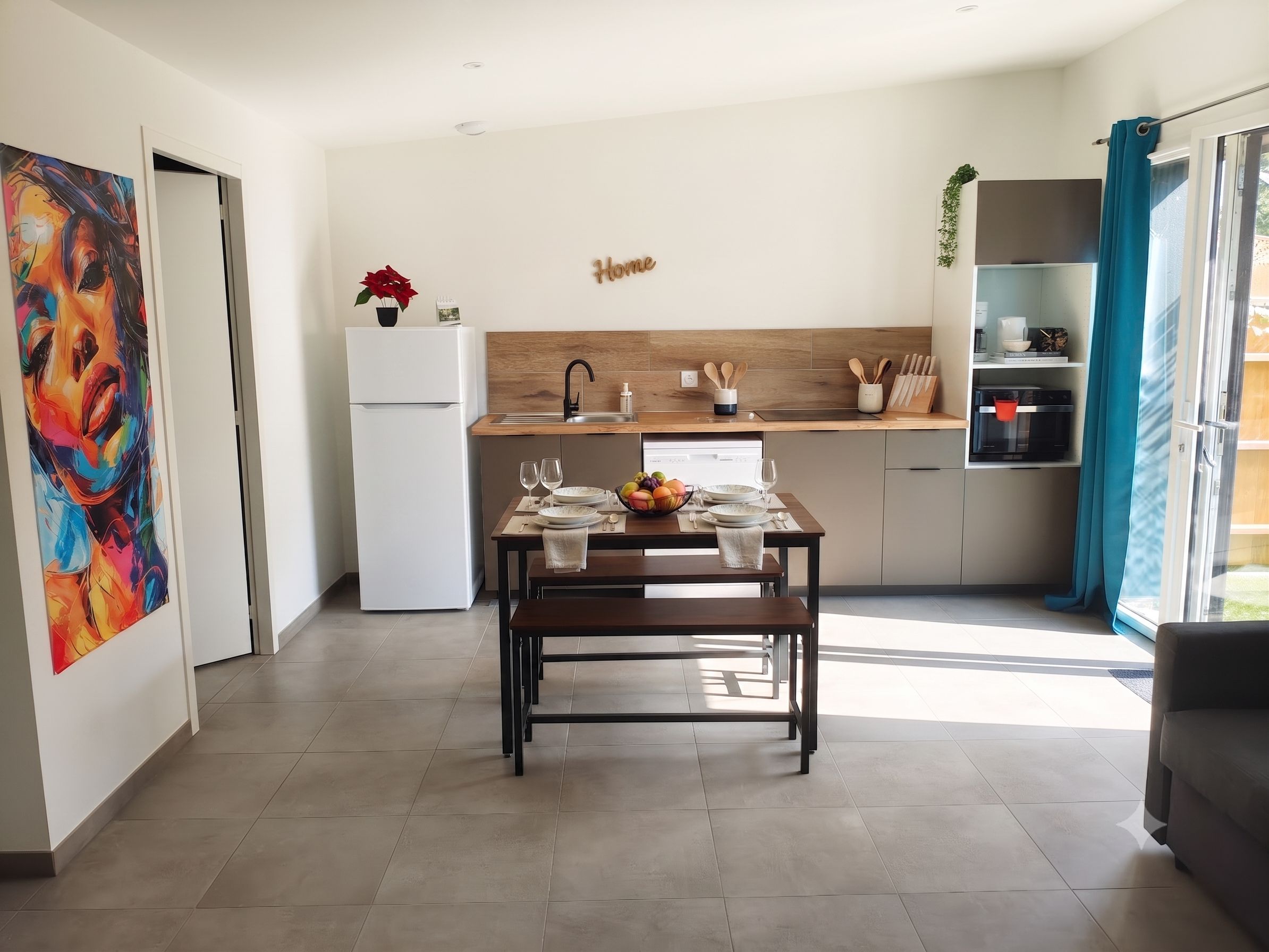 A modern kitchen with a dining table set for two, a refrigerator, and a coffee machine.
