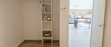 A hotel room with a wooden floor, a white wardrobe, a small kitchen area, and a bed with a neatly folded white towel.