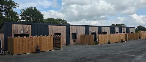 A row of wooden buildings with multiple doors, likely a commercial property with a paved parking area.