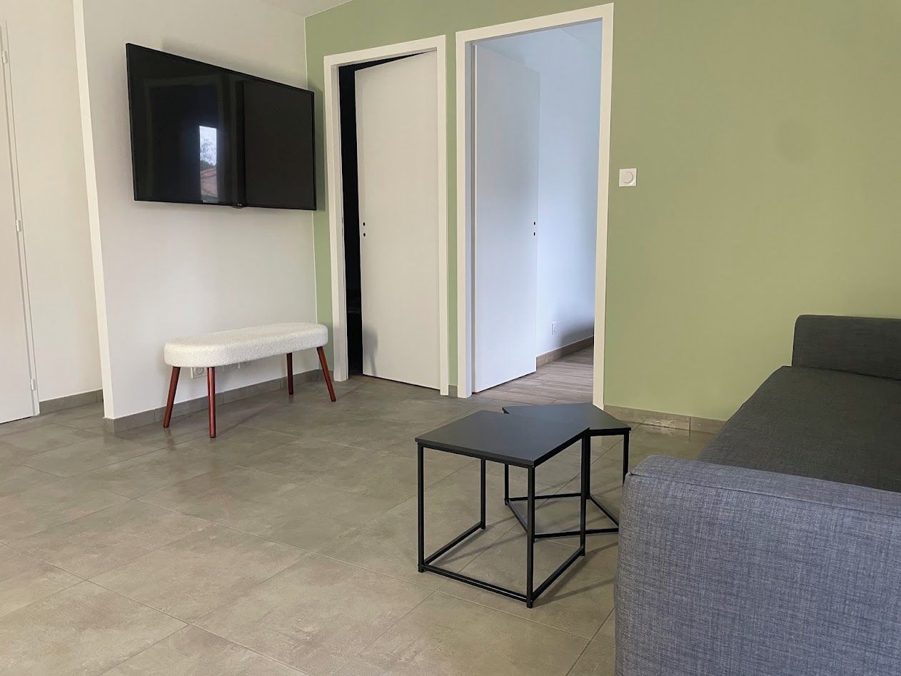 Um quarto com um banco, uma mesa, um sofá, uma televisão e uma porta.