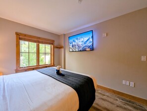 A hotel room with a bed, a window, a wall-mounted TV, and a wooden floor. - Prime Location | Steps to Slopes | King Bed (Keystone)